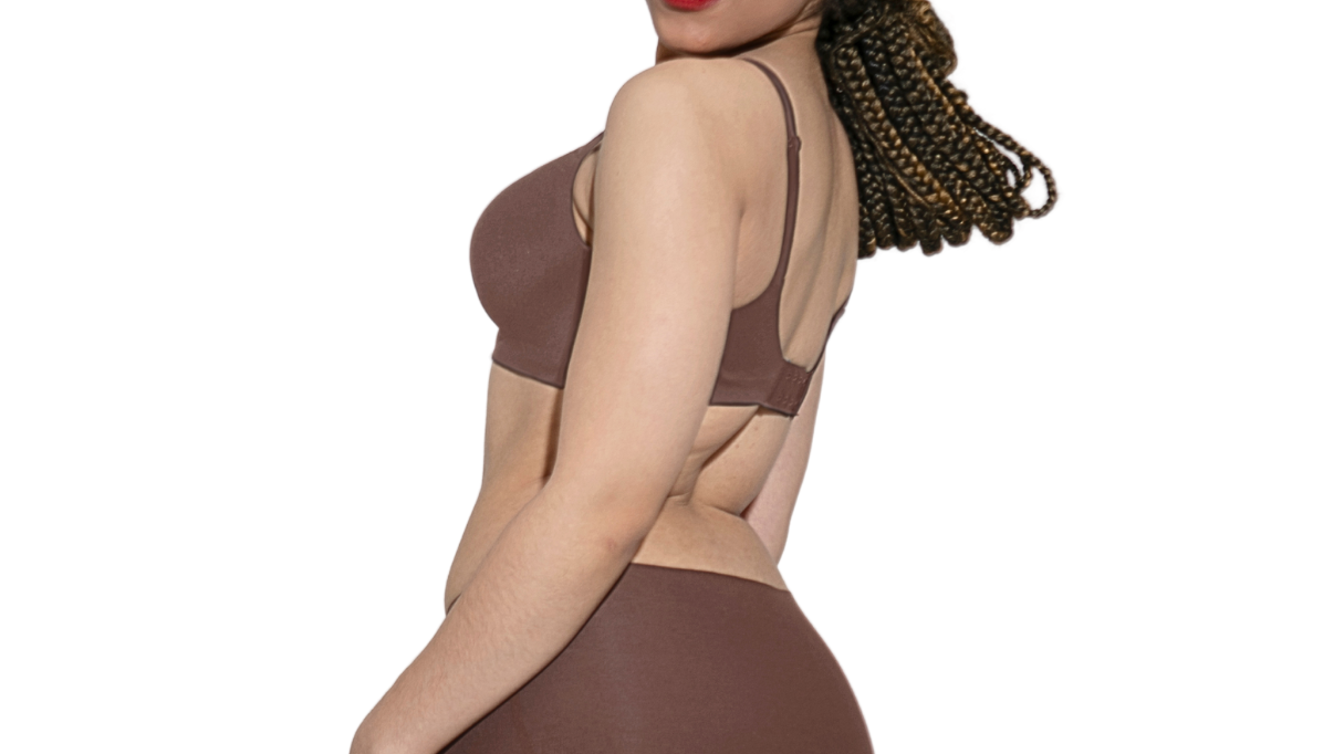 A bright, minimal lifestyle shot showing a woman confidently wearing fitted trousers with no panty lines, holding a reusable tote.